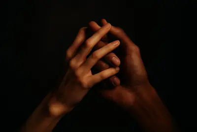 Two hands gently intertwined in warm light against darkness