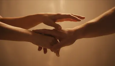 A hand gently guiding another by the wrist in warm amber light